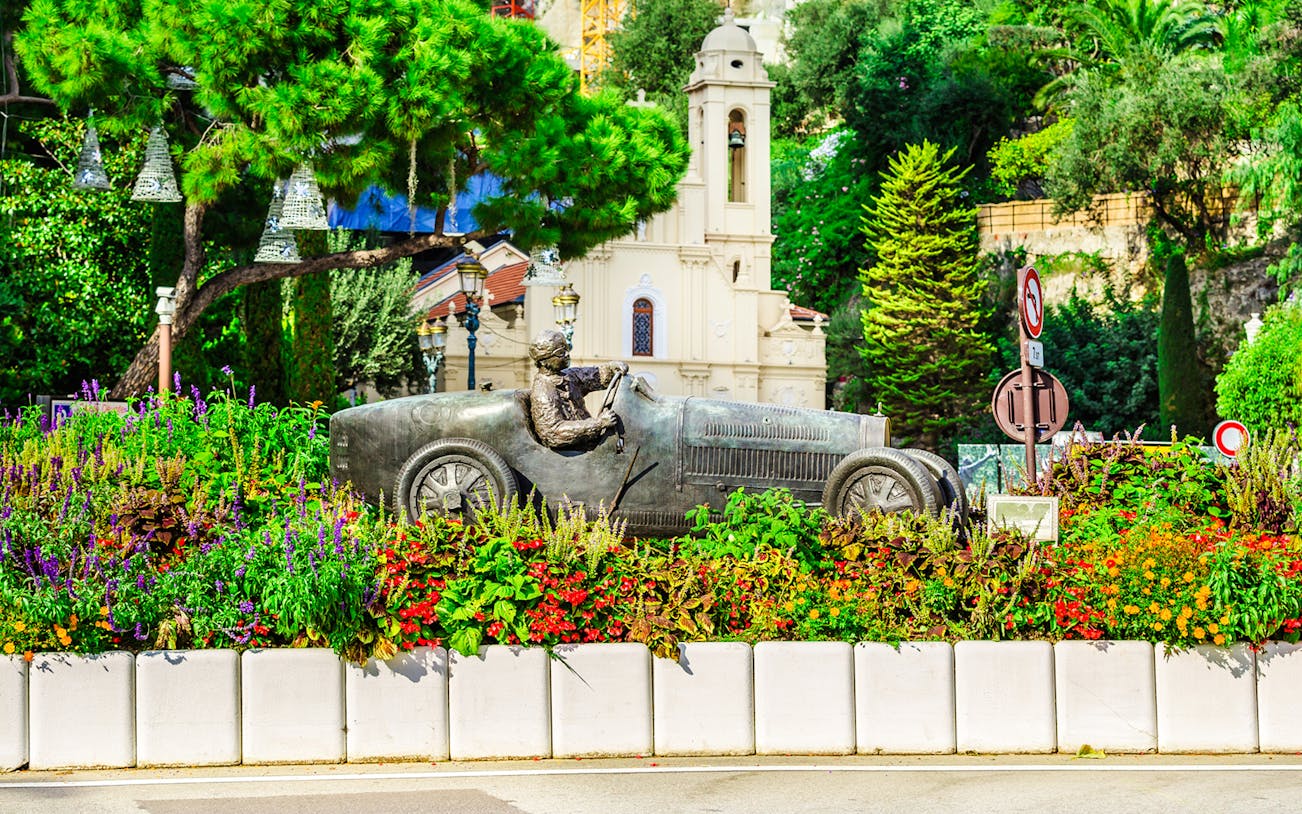 Bronze race car statue surrounded by flowers on Monaco Formula 1 Walking Tour.