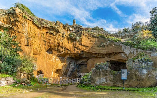 Entrance to the archaeological park of Cumae, Italy, featuring ancient rock formations.