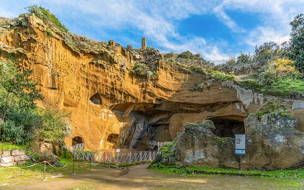 Entrance to the archaeological park of Cumae, Italy, featuring ancient rock formations.