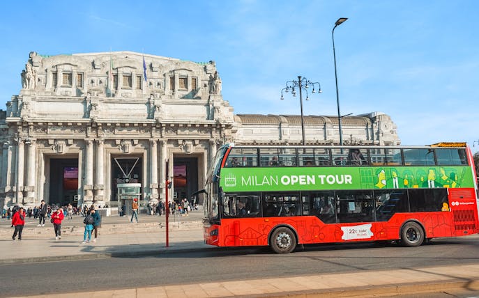 Hop-on hop-off tour bus in front of Milan Central Station.