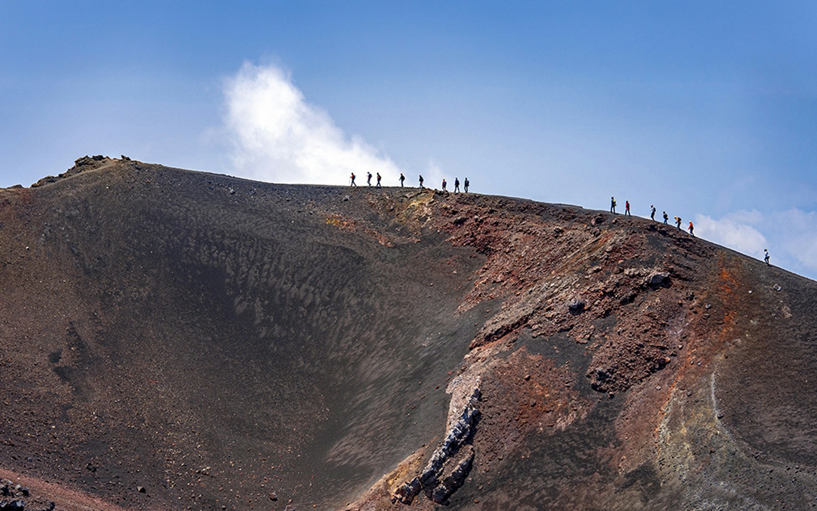 Hikers ascending Mount Etna summit under clear sky.