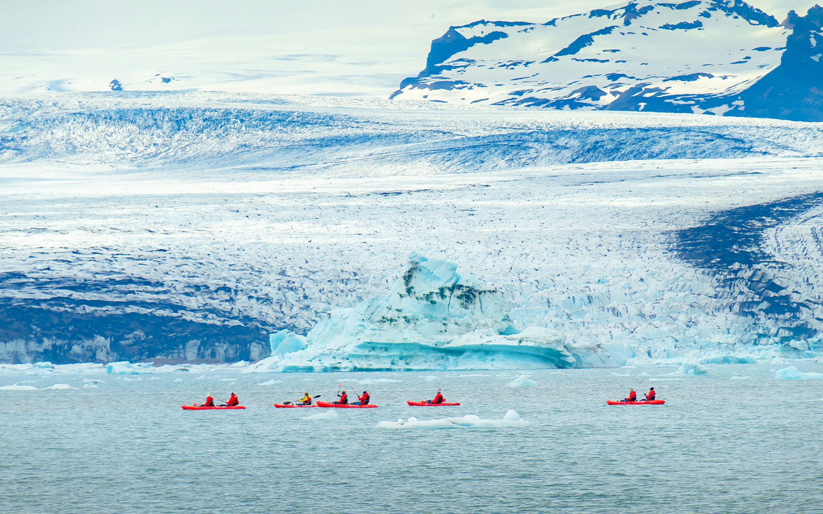 Friends kayaking in red kayaks near Jökulsárlón glacier lagoon, Iceland.