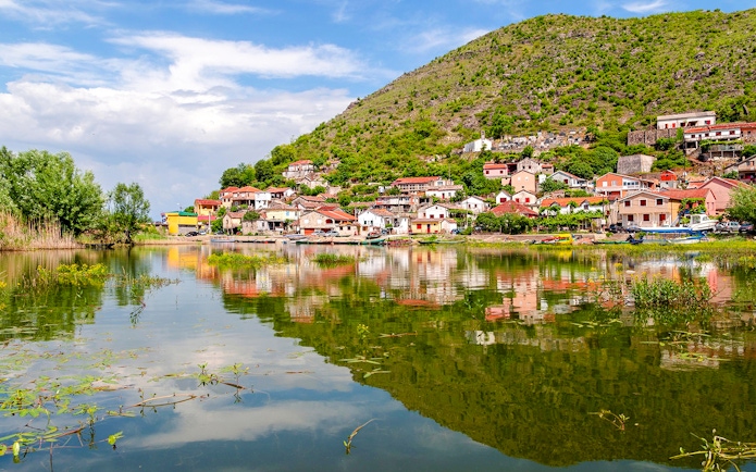 Village by Lake Skadar with hillside houses reflecting in the water.
