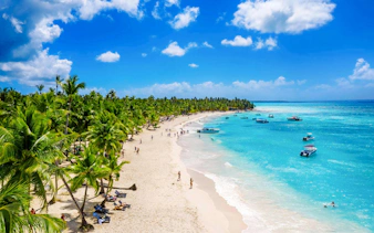 Saona Island beach with palm trees, tourists, and boats on turquoise water.