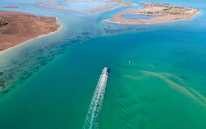 Aerial view of a cruise ship sailing through turquoise waters near coastal islands.