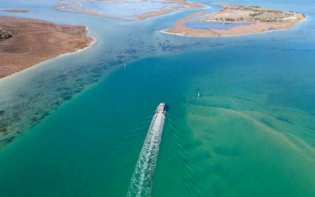 Aerial view of a cruise ship sailing through turquoise waters near coastal islands.