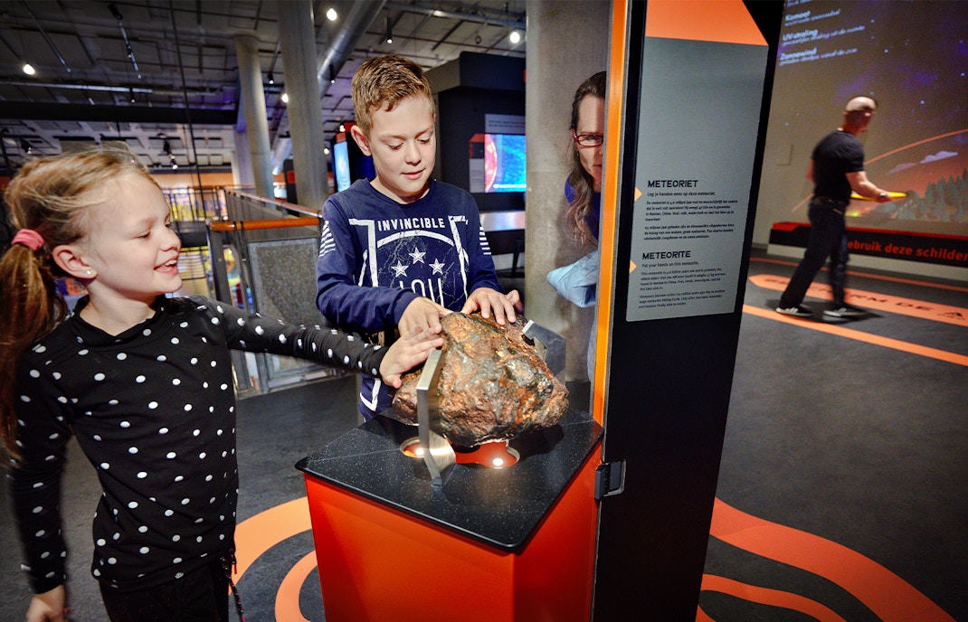 Children exploring a meteorite exhibit at NEMO Science Museum, Amsterdam.