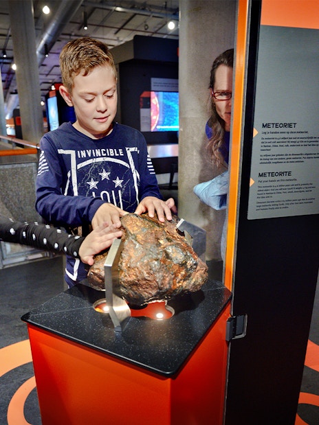 Children exploring a meteorite exhibit at NEMO Science Museum, Amsterdam.