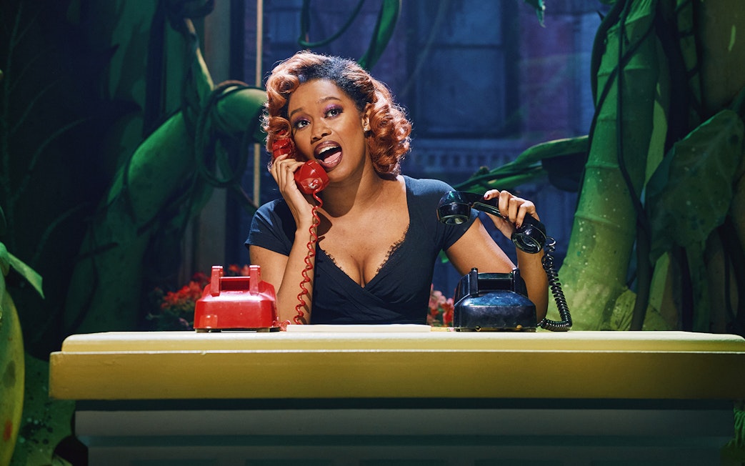 Performer on stage with red and black telephones in Little Shop of Horrors set.