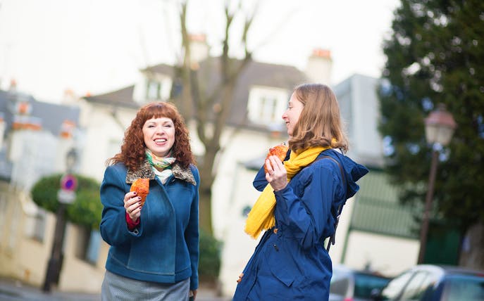 Two women enjoying pastries on a Paris street during a gourmet food tour.