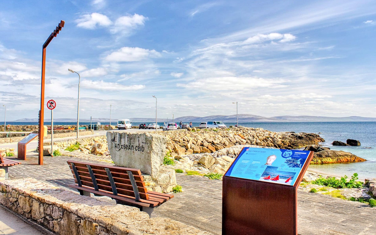 Spiddal's Old Quay with stone benches and informational sign, overlooking Galway Bay, Ireland.