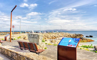 Spiddal's Old Quay with stone benches and informational sign, overlooking Galway Bay, Ireland.