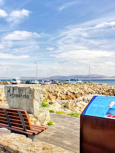 Spiddal's Old Quay with stone benches and informational sign, overlooking Galway Bay, Ireland.