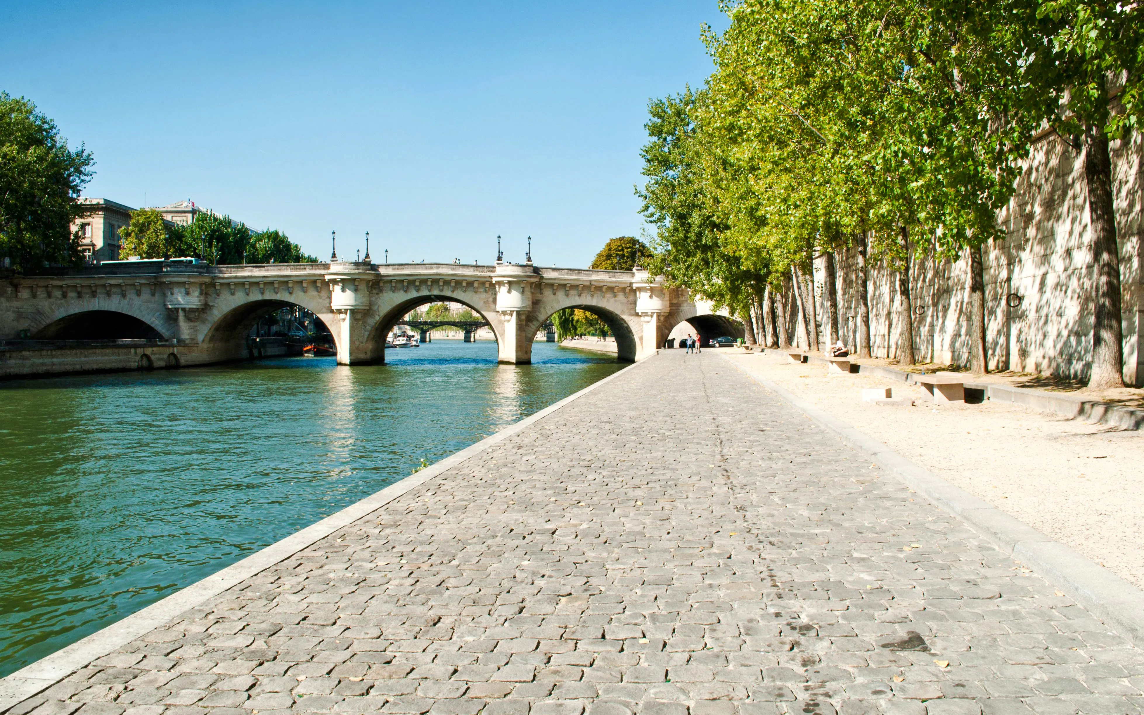 Pont Neuf bridge over the Seine River in Paris with tree-lined walkway.