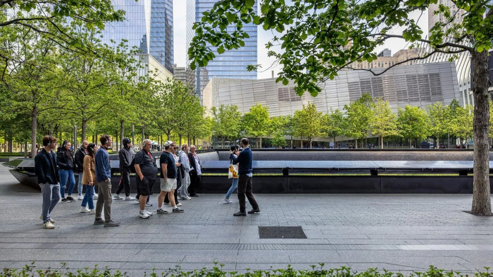 Visitors on a guided tour at the 9/11 Memorial, New York City, with museum exterior in view.