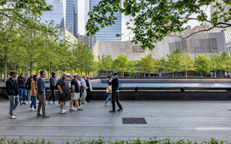 Visitors on a guided tour at the 9/11 Memorial, New York City, with museum exterior in view.