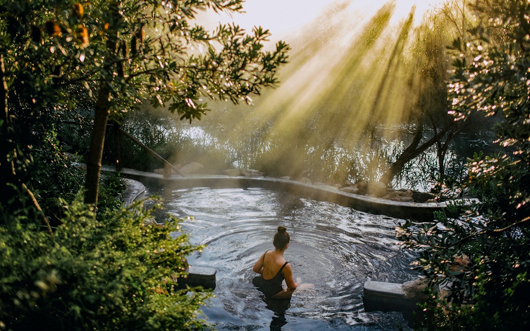 Person relaxing in a hot spring surrounded by lush greenery at Peninsula Hot Springs.