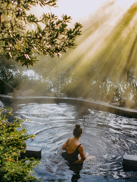 Person relaxing in a hot spring surrounded by lush greenery at Peninsula Hot Springs.