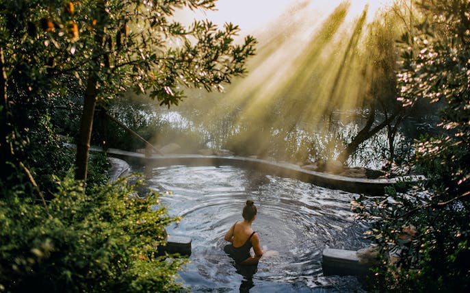 Person relaxing in a hot spring surrounded by lush greenery at Peninsula Hot Springs.