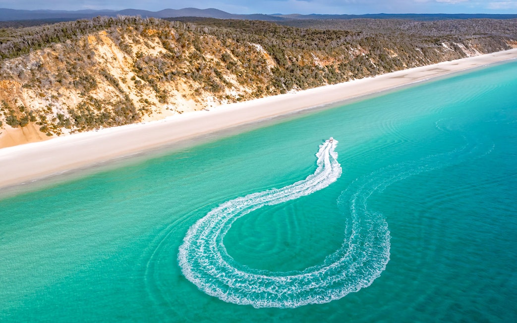 Tour boat creating a wake in turquoise water near Hervey Bay beach.