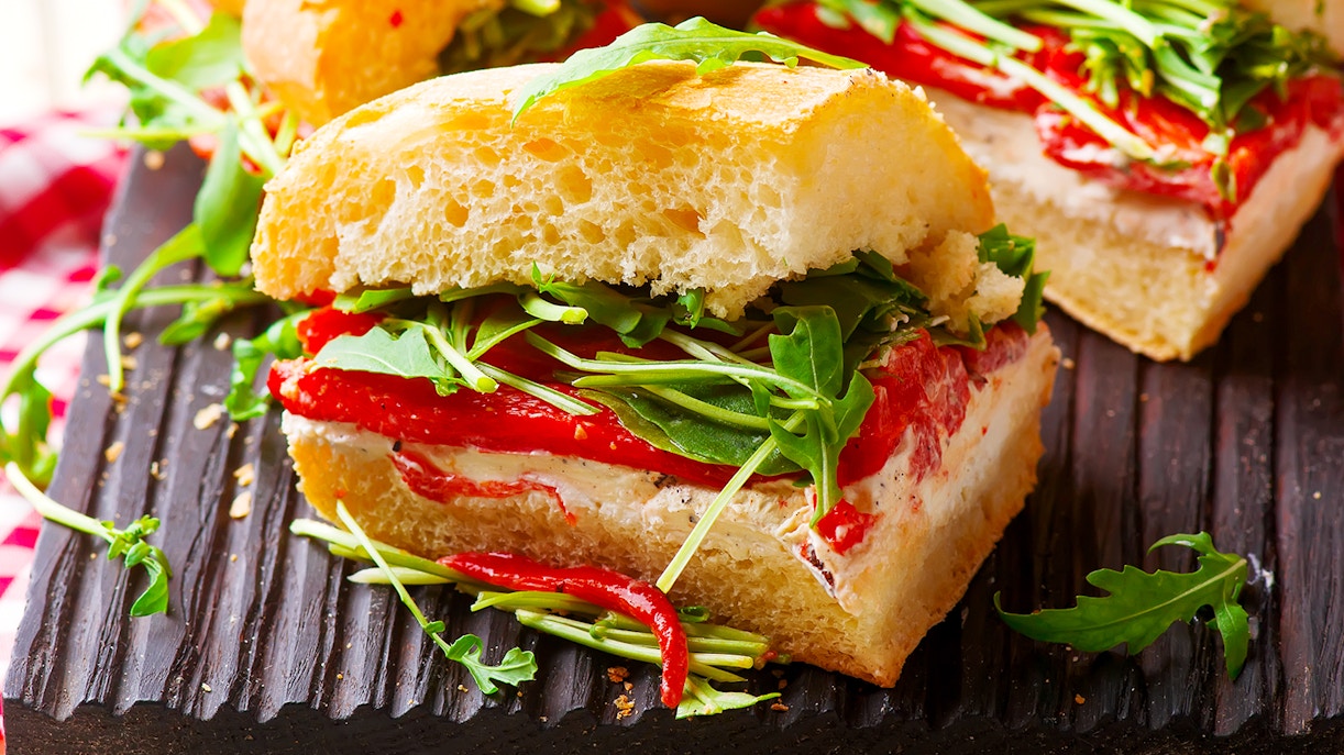Focaccia sandwich with roasted red peppers and arugula on a wooden board.