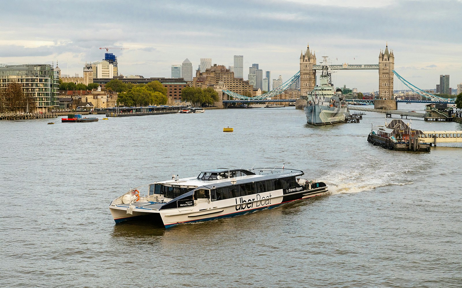 Thames River Uber Boat cruising past London's iconic Tower Bridge.