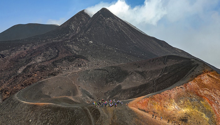 Hikers ascending Mount Etna summit with volcanic landscape in Sicily, Italy.
