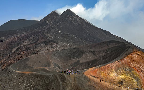 Hikers ascending Mount Etna summit with volcanic landscape in Sicily, Italy.