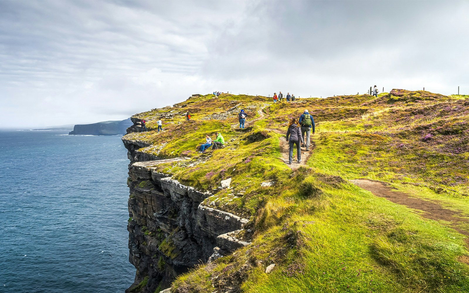 Tourists hiking along the Cliffs of Moher, Ireland, with ocean views.