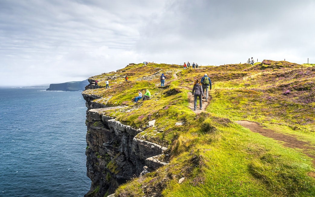 Tourists hiking along the Cliffs of Moher, Ireland, with ocean views.