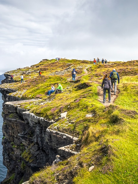 Tourists hiking along the Cliffs of Moher, Ireland, with ocean views.