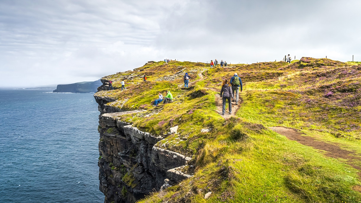 Tourists hiking along the Cliffs of Moher, Ireland, with ocean views.