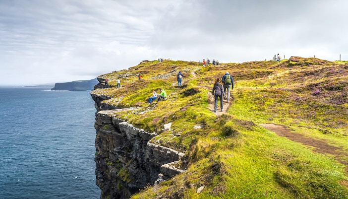 Tourists hiking along the Cliffs of Moher, Ireland, with ocean views.