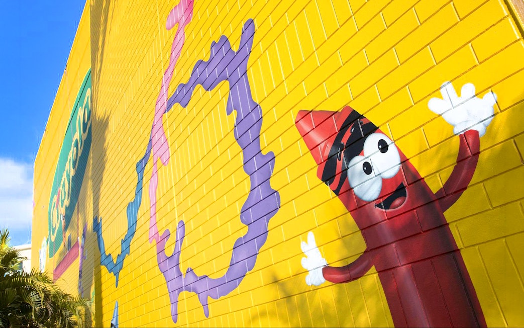 Colorful mural with Crayola crayon character on yellow wall at Crayola Experience, Orlando.