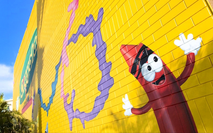 Colorful mural with Crayola crayon character on yellow wall at Crayola Experience, Orlando.