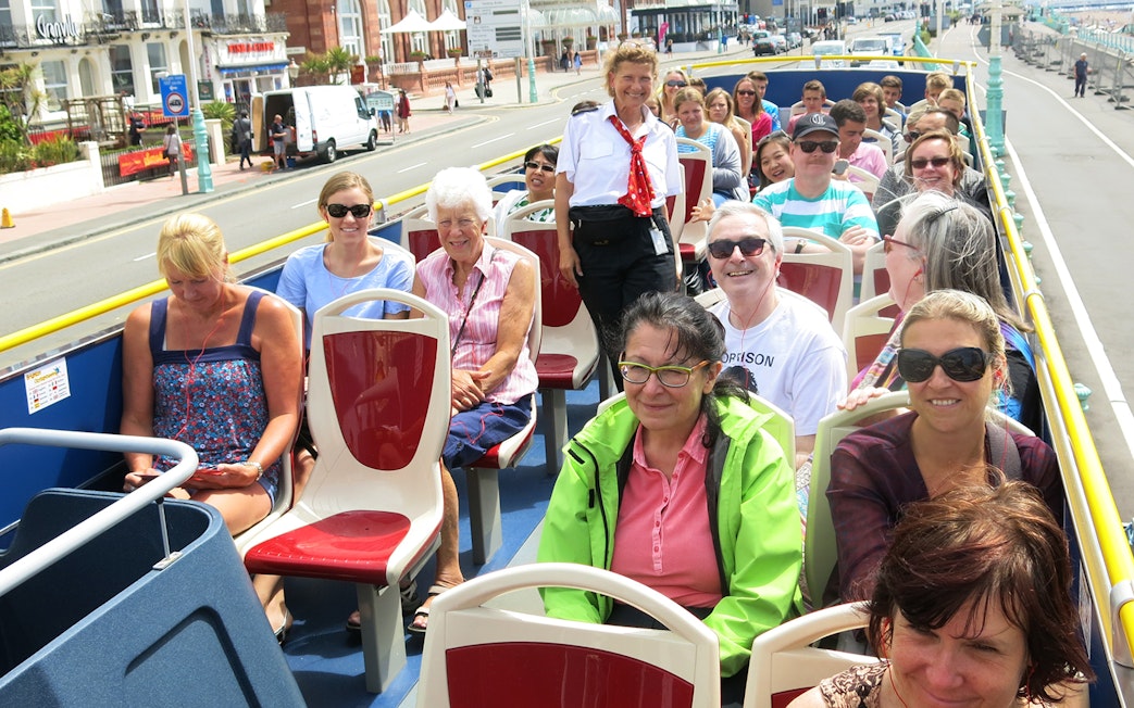 Tourists enjoying Brighton Hop-On Hop-Off bus tour along the seafront.