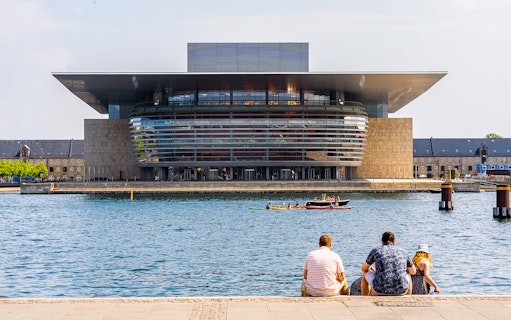 Royal Opera House in Copenhagen with people sitting by the waterfront and kayakers in the canal.