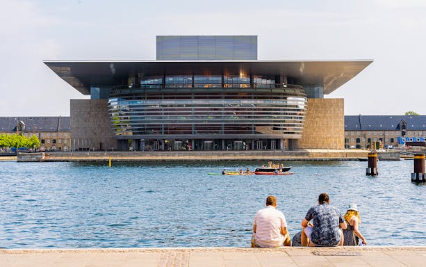 Royal Opera House in Copenhagen with people sitting by the waterfront and kayakers in the canal.