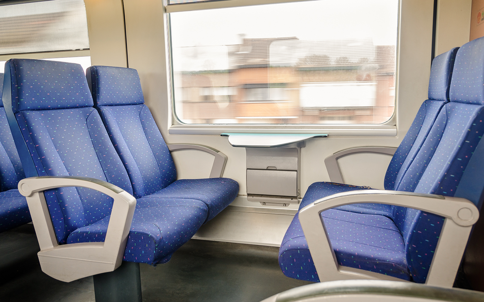 Train interior with blue seats and a window view of passing buildings.