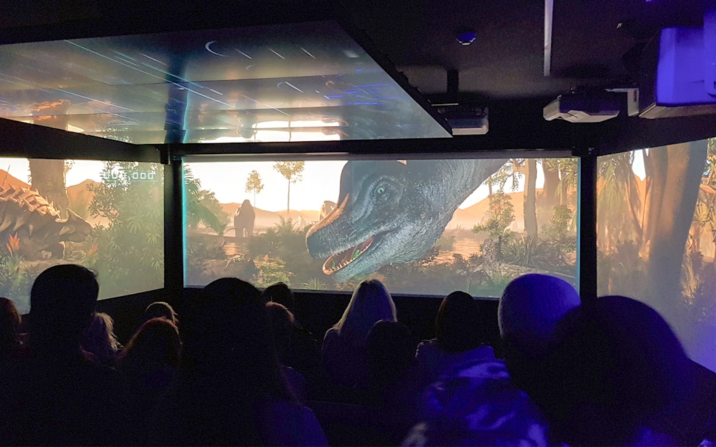 Audience watching an immersive underwater theatre experience with dinosaurs on screen.