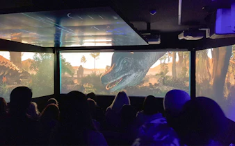 Audience watching an immersive underwater theatre experience with dinosaurs on screen.