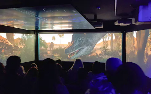 Audience watching an immersive underwater theatre experience with dinosaurs on screen.