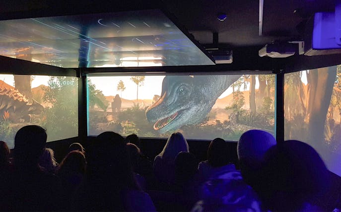 Audience watching an immersive underwater theatre experience with dinosaurs on screen.