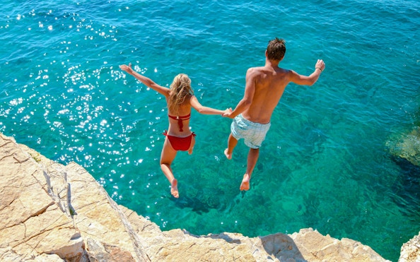 Couple cliff jumping into the Adriatic Sea, Croatia.