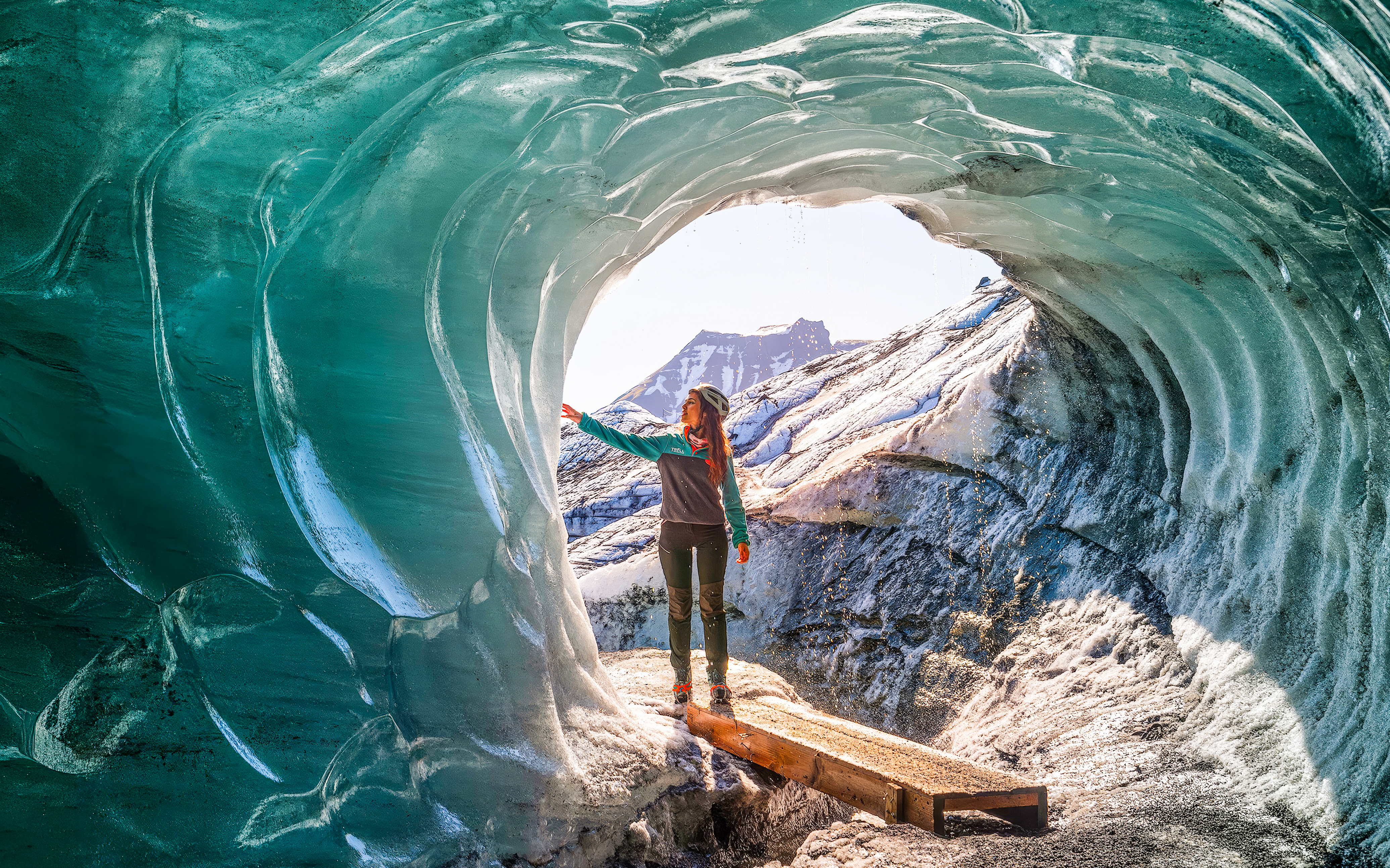 Person exploring inside Katla Ice Cave, Iceland, touching icy walls.