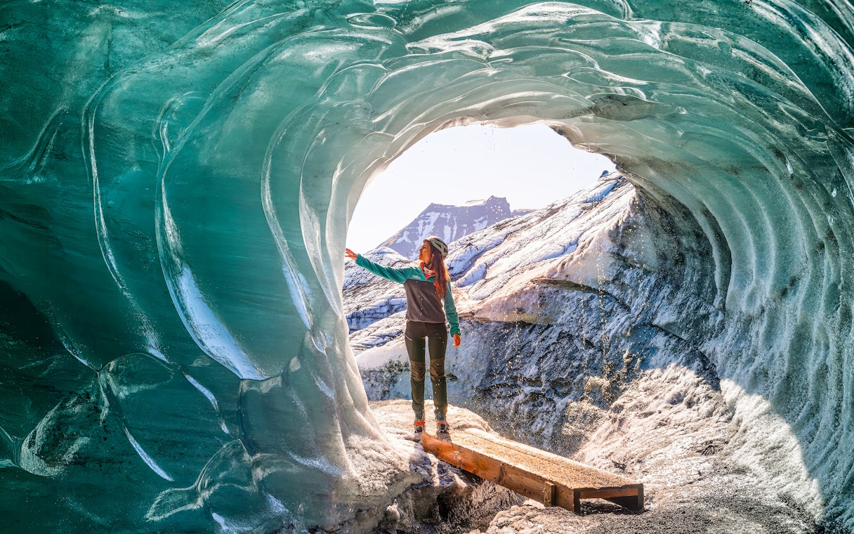 Person exploring inside Katla Ice Cave, Iceland, touching icy walls.