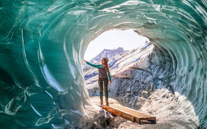 Person exploring inside Katla Ice Cave, Iceland, touching icy walls.