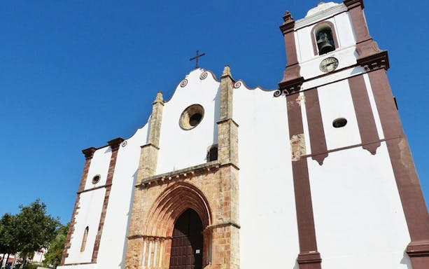 Historic church facade in Algarve, Portugal, featuring arched doorway and bell tower.