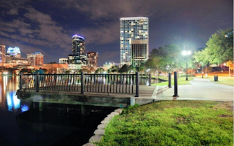 Orlando skyline at night with illuminated buildings and a lakeside walkway.