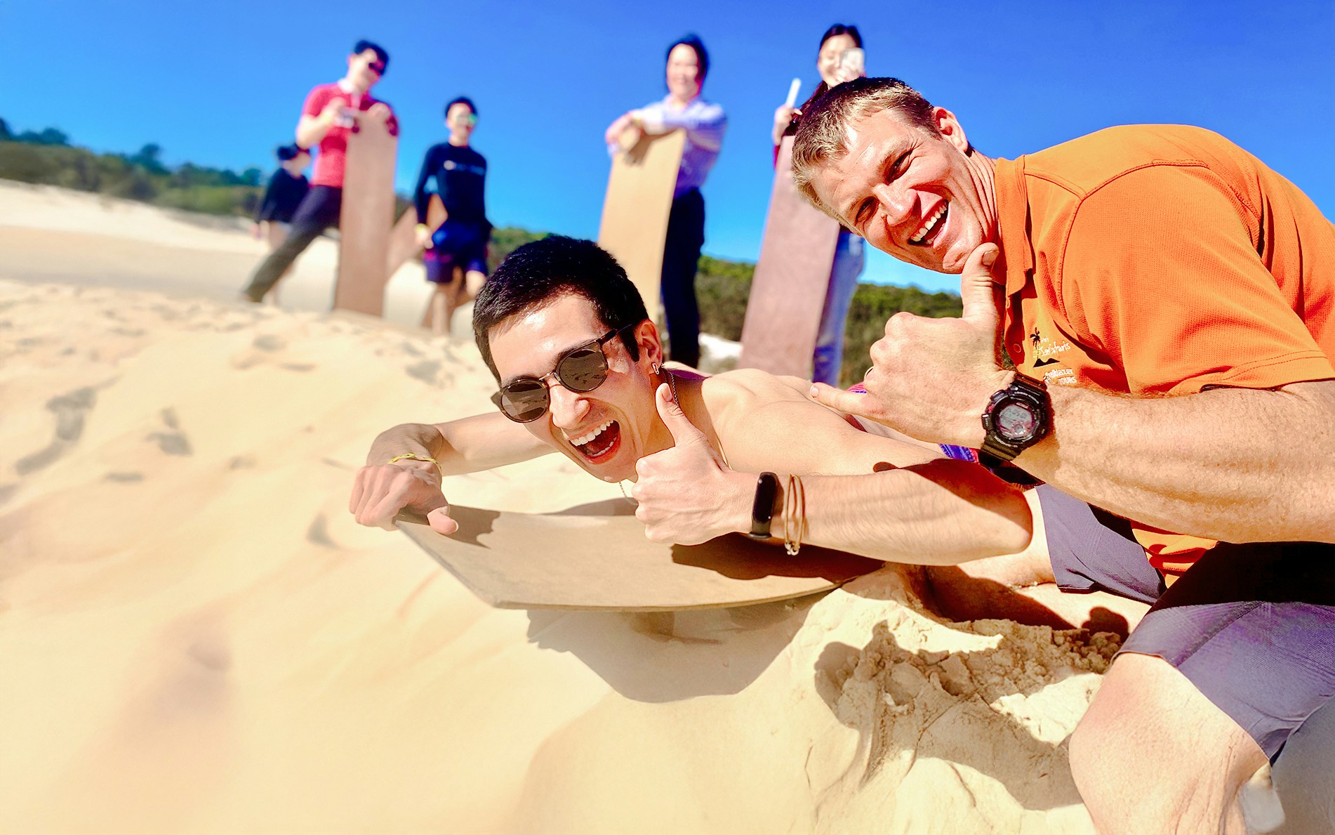 Man sand tobogganing on Moreton Island with group in background.